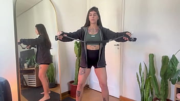 Flexing Her Inked Curves, She Stretches The Rubber Band Taut, Warming Up For A Deeper, Stronger Workout.